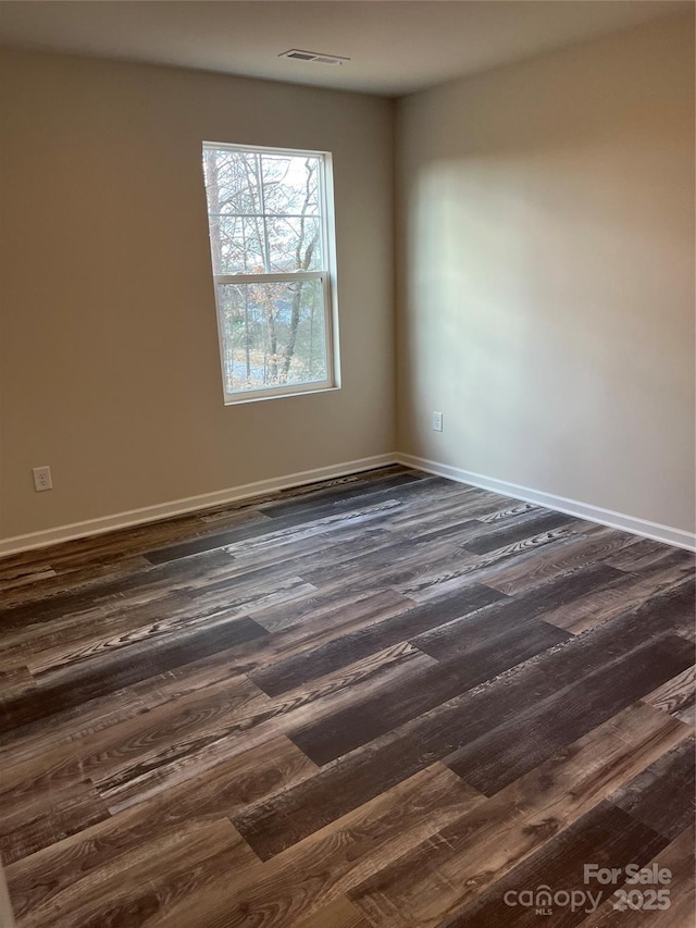 spare room featuring dark wood finished floors, visible vents, and baseboards