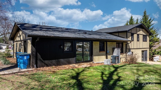 back of property featuring a yard, central AC unit, brick siding, and roof with shingles