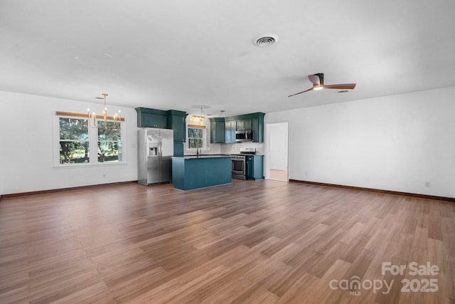 unfurnished living room with visible vents, light wood-style flooring, ceiling fan with notable chandelier, a sink, and baseboards