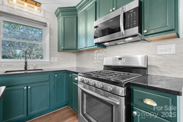 kitchen with tasteful backsplash, a sink, wood finished floors, stainless steel appliances, and green cabinetry