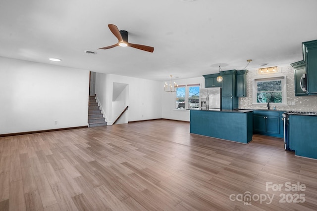 unfurnished living room featuring visible vents, ceiling fan with notable chandelier, a sink, light wood finished floors, and baseboards