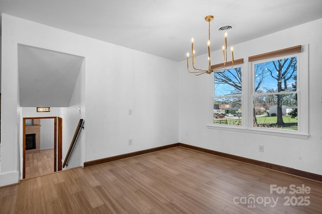 unfurnished dining area with wood finished floors, baseboards, visible vents, a glass covered fireplace, and a chandelier