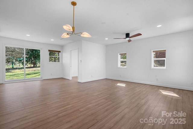 unfurnished living room with ceiling fan with notable chandelier, recessed lighting, wood finished floors, and baseboards