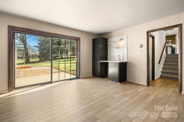 unfurnished living room featuring a sink, light wood-type flooring, baseboards, and stairs