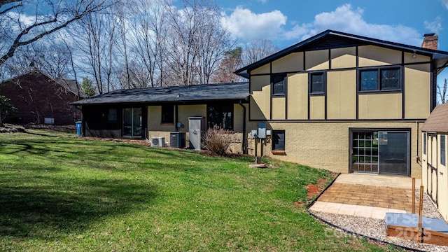 rear view of property featuring a lawn, central AC, brick siding, a chimney, and a patio area