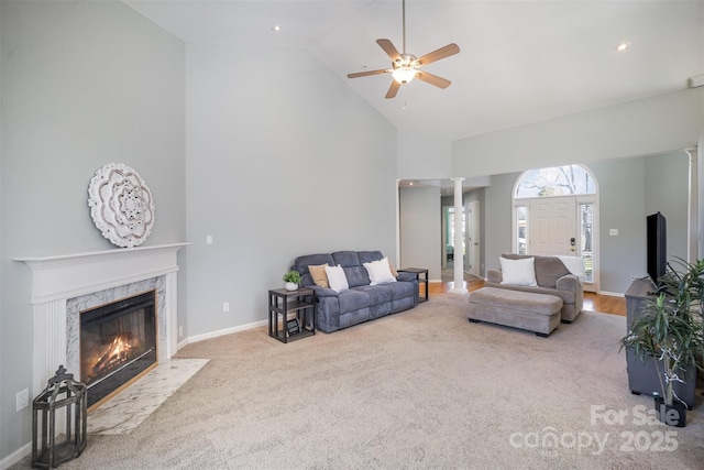 living room with high vaulted ceiling, carpet floors, a high end fireplace, baseboards, and ornate columns