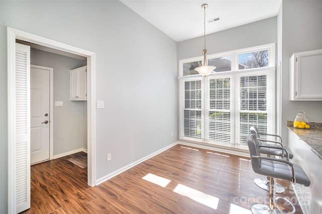 unfurnished dining area with dark wood-style flooring, visible vents, and baseboards