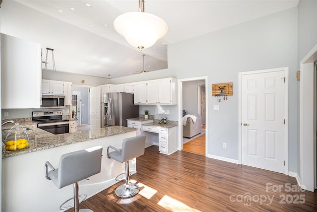 kitchen featuring dark wood-style floors, a peninsula, light stone countertops, vaulted ceiling, and stainless steel appliances