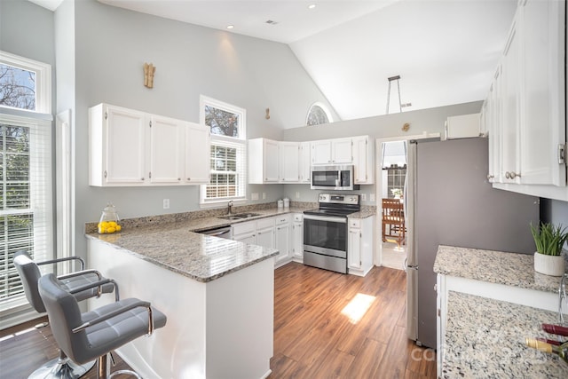 kitchen with light stone countertops, appliances with stainless steel finishes, white cabinets, wood finished floors, and a peninsula