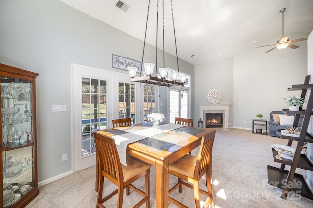 dining room with high vaulted ceiling, light colored carpet, a high end fireplace, baseboards, and visible vents