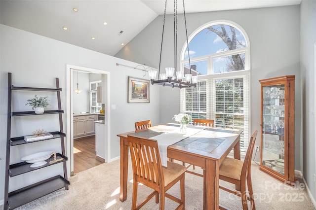 dining room with light carpet, high vaulted ceiling, baseboards, and an inviting chandelier