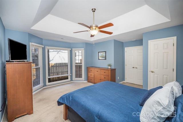 bedroom featuring baseboards, a tray ceiling, a ceiling fan, and light colored carpet