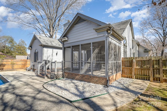 rear view of property featuring a patio, a sunroom, a fenced backyard, a chimney, and roof with shingles