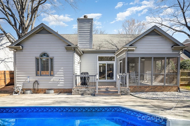 rear view of house featuring a fenced in pool, a patio, a chimney, a sunroom, and fence