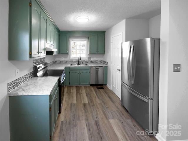 kitchen with a sink, stainless steel appliances, under cabinet range hood, and green cabinetry