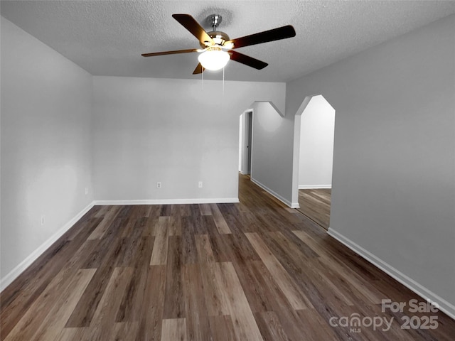 empty room with arched walkways, dark wood finished floors, baseboards, ceiling fan, and a textured ceiling