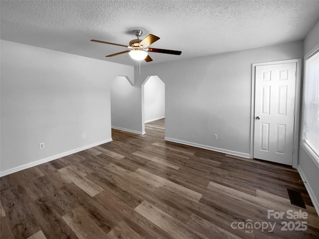 unfurnished room featuring a ceiling fan, visible vents, dark wood finished floors, and baseboards