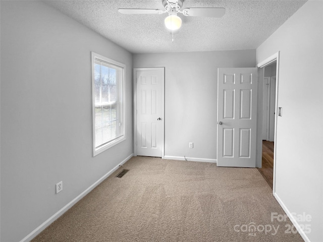 empty room with a textured ceiling, carpet flooring, a ceiling fan, visible vents, and baseboards