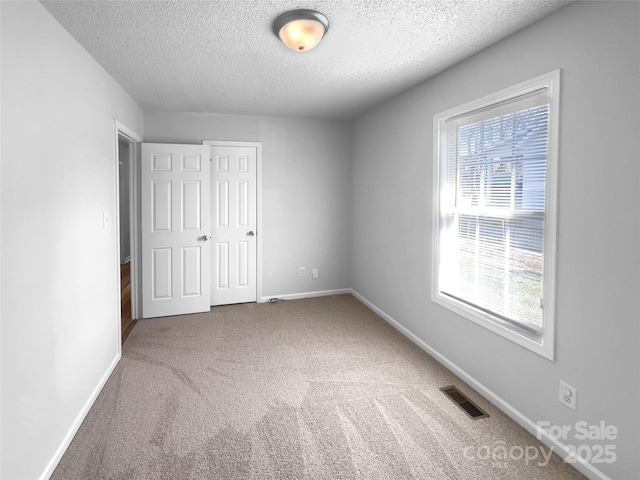 unfurnished bedroom with visible vents, baseboards, carpet, a textured ceiling, and a closet