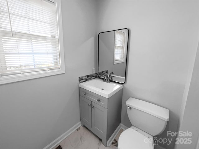 half bathroom with marble finish floor, toilet, vanity, and baseboards