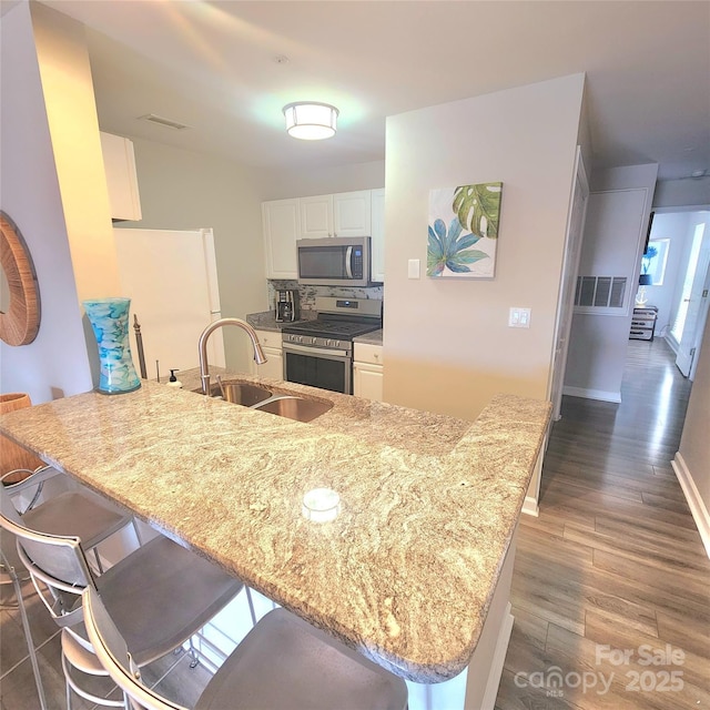 kitchen with a breakfast bar, a peninsula, wood finished floors, and appliances with stainless steel finishes