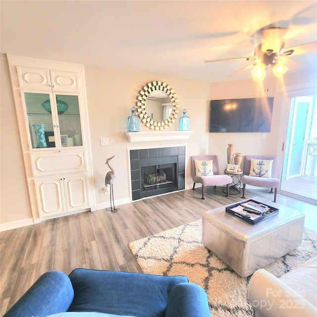 living area with a tile fireplace, baseboards, a ceiling fan, and wood finished floors