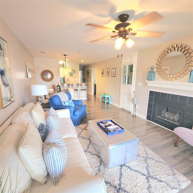 living area featuring a tiled fireplace, baseboards, ceiling fan, and wood finished floors