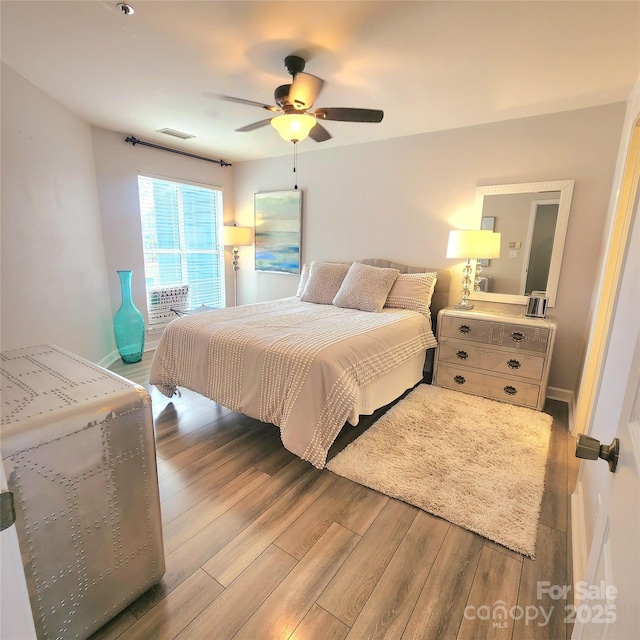 bedroom with ceiling fan, visible vents, baseboards, and wood finished floors