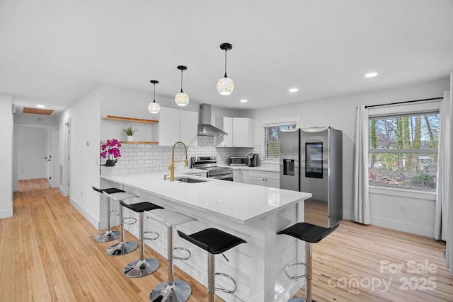 kitchen with a sink, a peninsula, appliances with stainless steel finishes, wall chimney exhaust hood, and light countertops