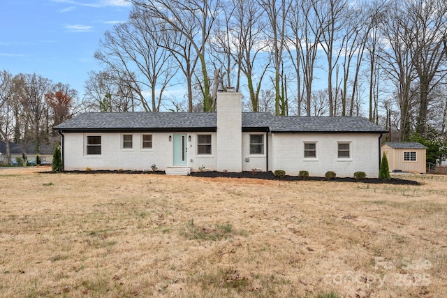 view of front of property featuring brick siding, a front lawn, a chimney, an outbuilding, and a storage unit