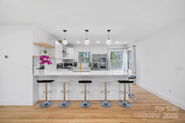 kitchen with a peninsula, light countertops, appliances with stainless steel finishes, a kitchen breakfast bar, and backsplash