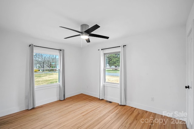 empty room featuring ceiling fan, visible vents, baseboards, and wood finished floors