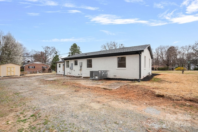 rear view of house featuring an outbuilding, a storage shed, crawl space, brick siding, and central AC unit