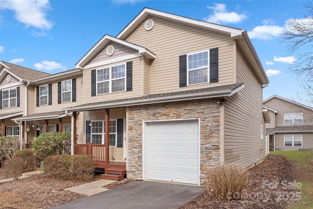 view of front of house featuring a garage, covered porch, stone siding, and driveway