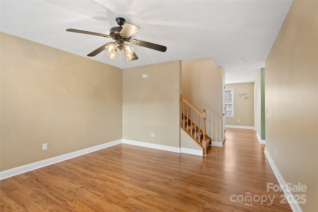 empty room with stairway, ceiling fan, baseboards, and wood finished floors