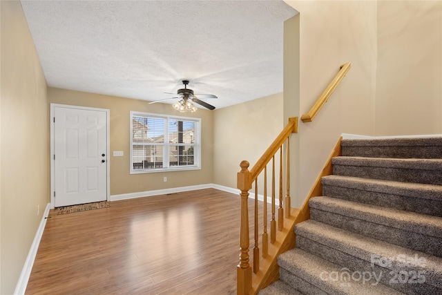 foyer entrance with a ceiling fan, a textured ceiling, wood finished floors, stairway, and baseboards