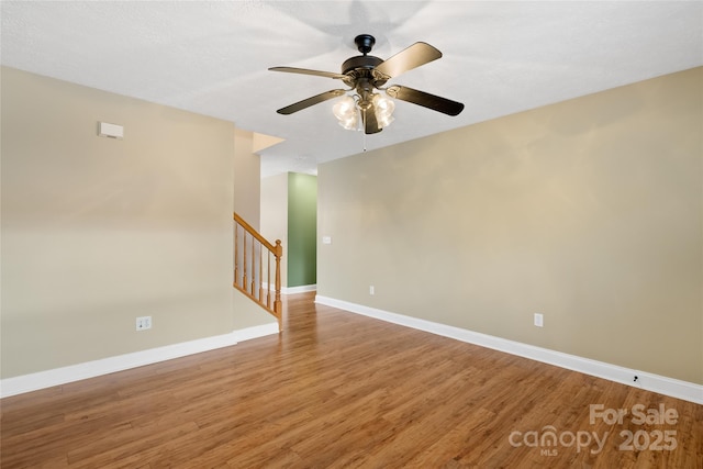 empty room featuring stairway, ceiling fan, baseboards, and light wood-style floors