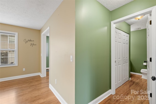 hallway with light wood finished floors, a textured ceiling, and baseboards