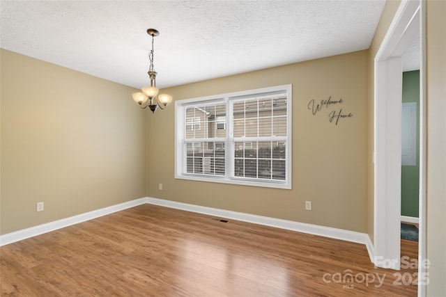 spare room featuring a chandelier, baseboards, a textured ceiling, and wood finished floors