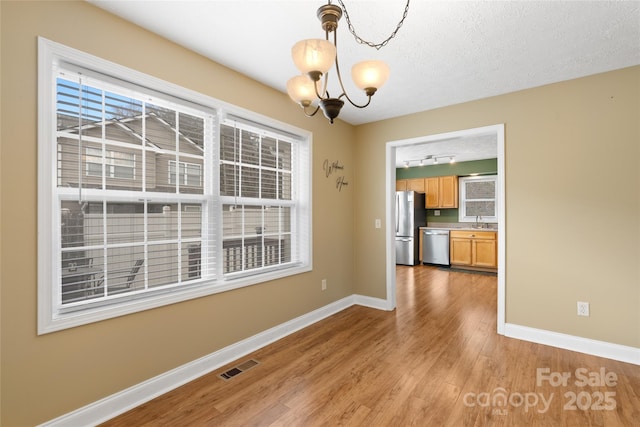 unfurnished dining area featuring light wood-style flooring, baseboards, visible vents, and a sink