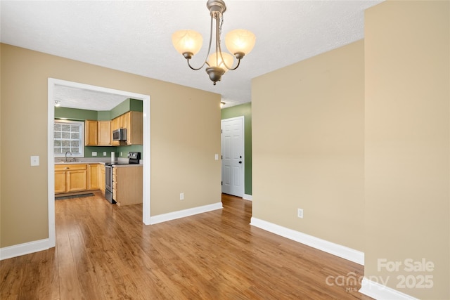 unfurnished dining area featuring light wood-style flooring, baseboards, an inviting chandelier, and a sink