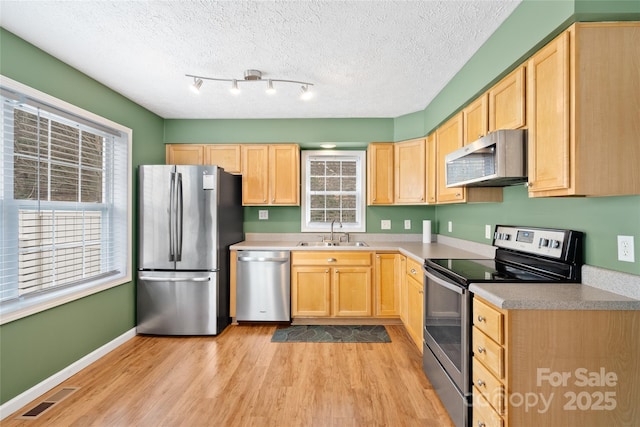 kitchen with visible vents, a sink, light brown cabinetry, stainless steel appliances, and light wood-style floors