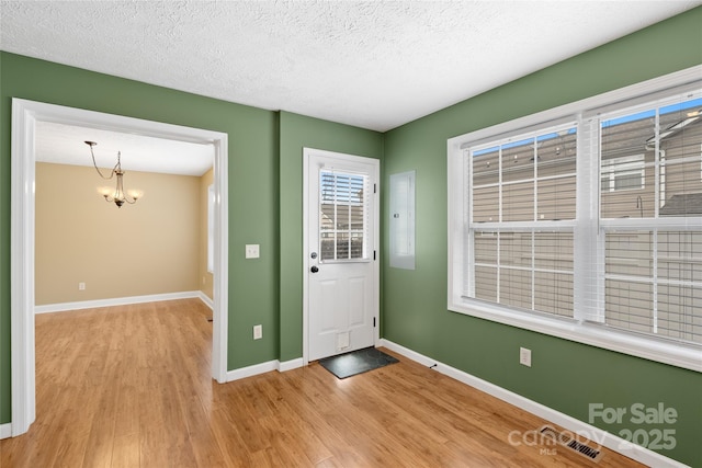 foyer entrance featuring light wood finished floors, visible vents, baseboards, a chandelier, and a textured ceiling