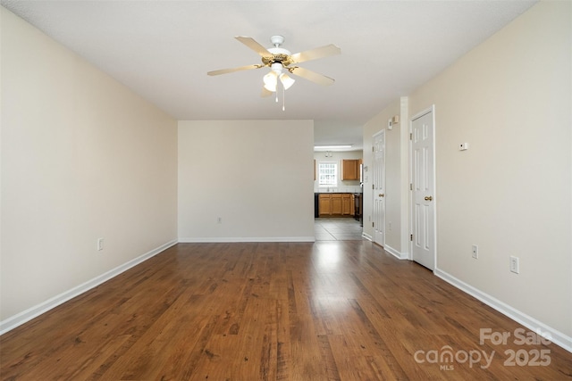 spare room featuring dark wood-type flooring, a ceiling fan, and baseboards