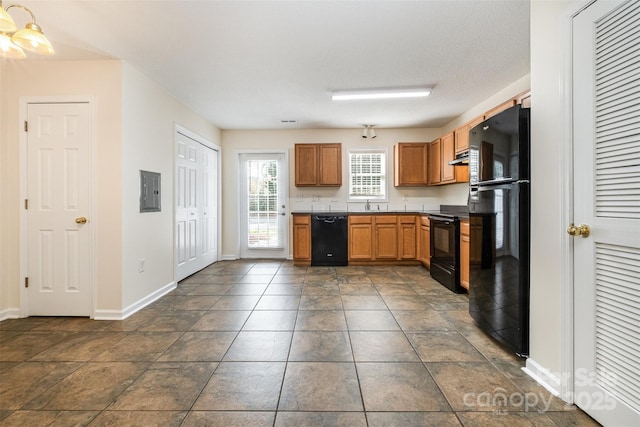 kitchen featuring baseboards, black appliances, under cabinet range hood, dark countertops, and brown cabinets