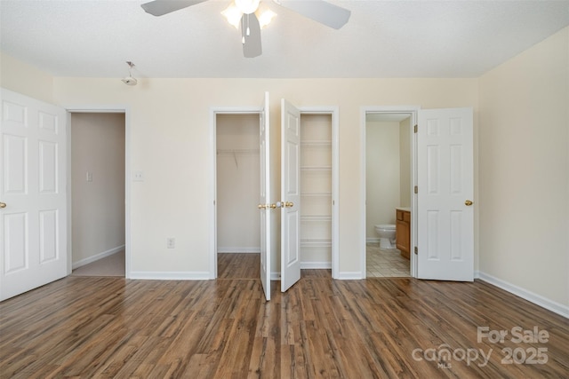 unfurnished bedroom with ensuite bathroom, a ceiling fan, wood finished floors, a closet, and baseboards