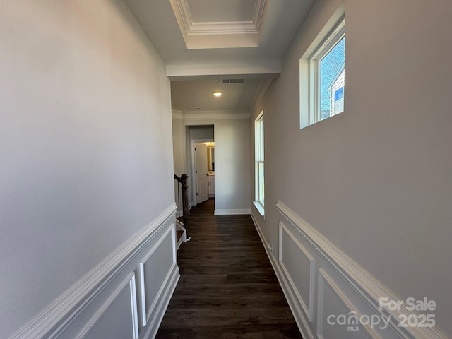 hallway with visible vents, wainscoting, dark wood-type flooring, crown molding, and a decorative wall