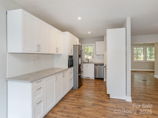 kitchen with stainless steel appliances, wood finished floors, a sink, and white cabinets