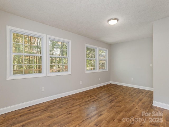 unfurnished room with a textured ceiling, wood finished floors, and baseboards