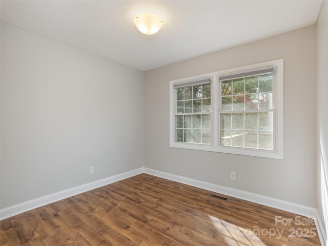 empty room featuring dark wood-type flooring, visible vents, and baseboards